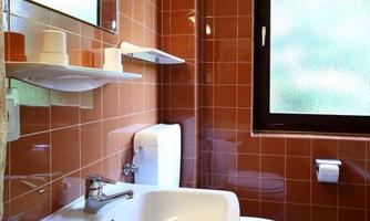 A modern bathroom with orange tiles. There is a sink, a toilet, and a window with a view outdoors.