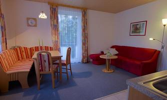 A cozy living area with a dining table, a red sofa, and a large window with curtains. The room is bright and inviting, perfect for relaxing hours.