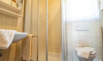 A modern bathroom with a shower and a bright window front. The walls are light tiled, and the wooden ceiling creates a warm atmosphere.