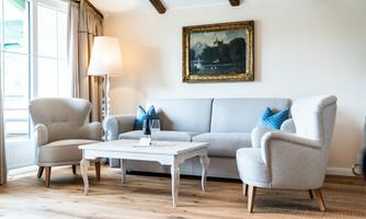 An inviting living room with a gray sofa and two comfortable chairs. The room is bright and has a larger window as well as a stylish lamp.