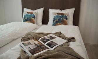 A cozy bedroom with two beds and colorful cushions. On the blanket lies a warm blanket and a magazine.