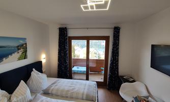 A modern room with two beds and a balcony. The room has large windows and is brightly furnished.