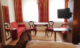 A cozy hotel room with a double bed, a table, and chairs. The room has large windows and a stylish decor in warm colors.