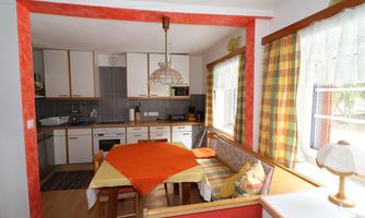 A modern kitchen with bright colors and a dining area. The table is decorated with an orange tablecloth and comfortable cushions.