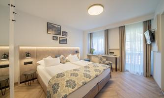 A modern bedroom with two single beds and stylish furnishings. Large windows provide plenty of natural light and a pleasant atmosphere.