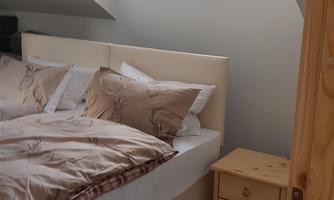 A cozy bedroom with a large bed and a wooden dresser. The window lets in plenty of daylight.