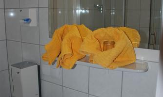 A bathroom with a sink and a mirror. Yellow towels are placed on a shelf.