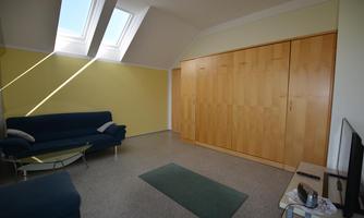 A bright living space with slanted windows and a blue couch. There is a large wooden cabinet on the wall.