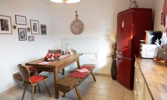 A cozy kitchen with a wooden table and a bench. The red refrigerator and the wall decoration give the room an inviting atmosphere.