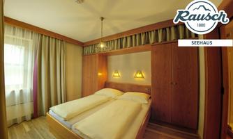 A cozy guest room with two single beds and warm wooden details. The windows are fitted with curtains that create a bright room.
