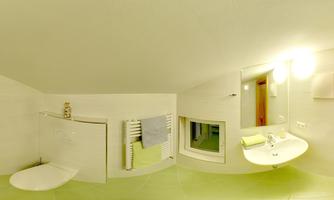 A modern bathroom with white walls and light green tiles. There is a sink, towels, and plenty of natural light.