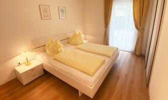 A bright bedroom with a double bed and two large pillows. Curtains in soft colors let in plenty of light.