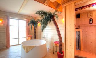 A modern bathroom with a freestanding bathtub and palm trees. In the background, there is a sauna and large windows that let in plenty of light.