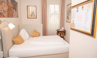 A cozy room with a single bed, decorated in soft colors. On the walls hang some pictures, and a small table stands next to the bed.