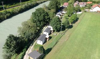 An overview of a sports field next to a river. In the background, some small houses and trees can be seen.