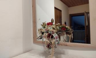 A beautiful floral arrangement with red roses is on a table. In the background, a mirror and a bright wall can be seen.