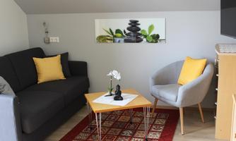 A cozy living room with a gray sofa and an armchair. On the table, there is a small plant and a Buddha figure.