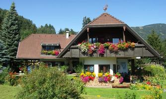A beautiful house in Alpine style surrounded by colorful flowers. The garden is well-maintained and the landscape offers a picturesque backdrop.