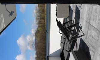 A modern balcony with comfortable seating and a beautiful view of the blue sky and nature. The atmosphere is calm and inviting.