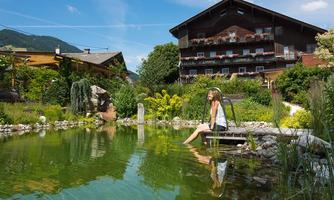 A beautiful garden with a clear pond and a relaxing atmosphere. In the background, you can see a traditional wooden house and lush plants.