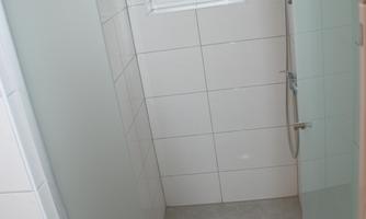 A modern bathroom with white tiles and a large mirror. There is a small window that lets in natural light.