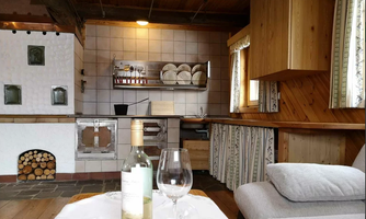 A cozy kitchen with wooden shelves and a traditional oven. On the table are a bottle of white wine and a glass.