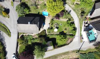 An aerial view of a house with a beautiful garden. Around the property, one can see pathways and a small pool area.