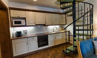 A modern kitchen with white cabinets and wood surfaces. A curved staircase leads to the upper floor.