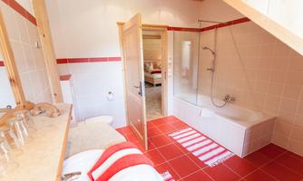 A modern bathroom with a bathtub and a shower. The walls are brightly tiled, and there are red accents in the design.