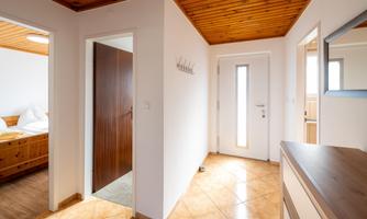 A bright hallway with a wooden ceiling and six doors. On the right side, there is a modern entrance door.