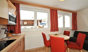 A bright and modern kitchen with a round table and red chairs. Large windows offer a view of the surrounding landscape.