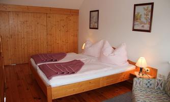 A cozy bedroom with a double bed and wood paneling. The room has pictures on the wall and a small couch.