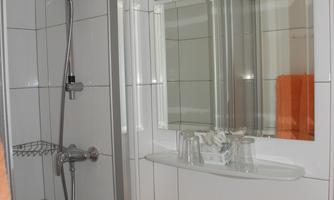 A modern bathroom with a shower and a sink. Orange towels are lying on the shelf.