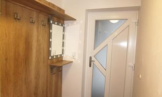A modern hallway with wooden furniture and a large mirror. The front door is made of glass and has a white design.