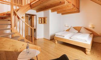 A modern bedroom with wooden decor and a cozy atmosphere. In the background, there is an elegant spiral staircase.