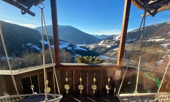 A cozy porch with hanging chairs and a view of snow-covered mountains. The sky is clear and blue.
