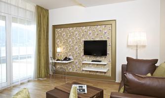 A modern living room with a TV on the wall and a cozy sofa. Large windows provide plenty of light and an inviting atmosphere.