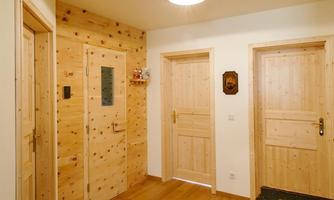 A bright hallway with wooden walls and doors. The floor is wooden and there is a ceiling lamp.
