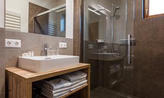 A modern bathroom with a glass shower and a wooden vanity. The walls are in warm brown tones, and there is a large mirror.