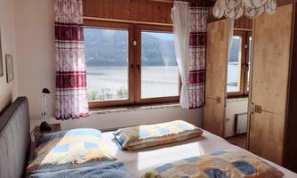 A cozy bedroom with a double bed and colorful cushions. Through the windows, there is a beautiful view of the lake and the mountains.