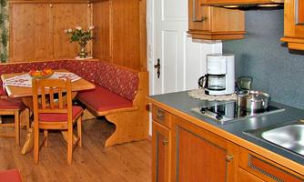 A cozy kitchen with wooden cabinets and a dining table. In the background, there is a seating area with red cushions.