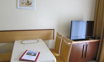 A simple room with a table, chairs, and a television. A picture hangs on the wall and the windows are covered with curtains.