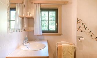 A bright bathroom with a round sink and a large window. There are towels and modern decor on the wall.