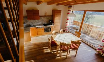 A bright and cozy kitchen with wooden furniture and a dining area. Large windows offer a view of the landscape.