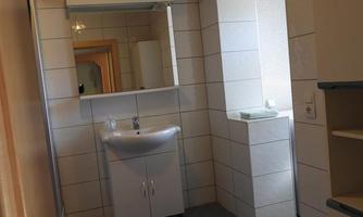 A modern bathroom with bright tiles and a sink. The room has a wooden ceiling and a blue bath mat.
