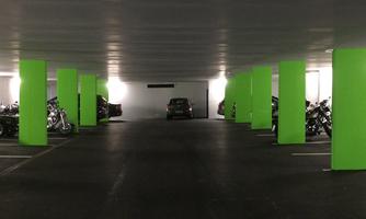 A parking lot with green pillars and several motorcycles. In the background, there is a car.