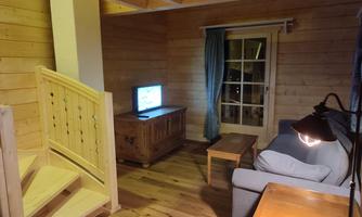 A cozy living space with wooden paneling and a staircase. A couch, a table, and a television are visible, as well as a window with curtains.