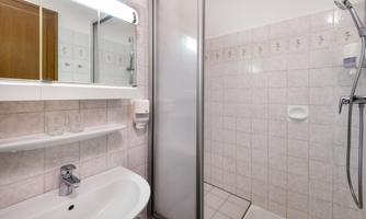 A modern bathroom with a separate shower and a sink. The walls are tiled in a light color, and there is a large mirror.