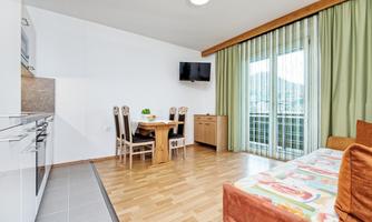 A modern living kitchen with a dining area and a balcony. Bright colors and large windows create plenty of light.