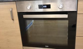 A modern oven with a stainless steel front in a bright kitchen. The oven is integrated into a wooden cabinet wall.